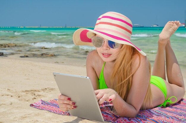 Schöne Frau mit Bikini und Hut schläft am Strand mit Tablet