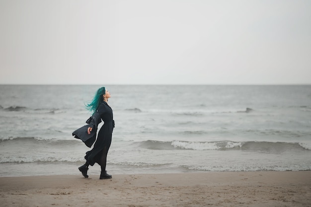 Schöne Frau mit blauen Haaren geht am Meer entlang und genießt den Wind