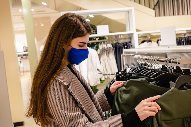 Schöne Frau mit blauer Gesichtsmaske kauft Kleidung im Einkaufszentrum ein