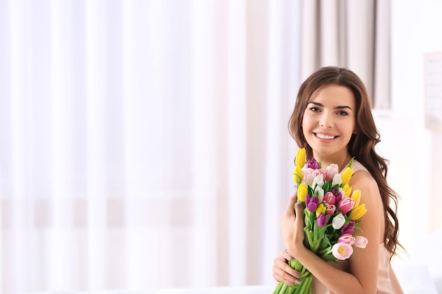 Schöne Frau mit Blumenstrauß aus Tulpen zu Hause