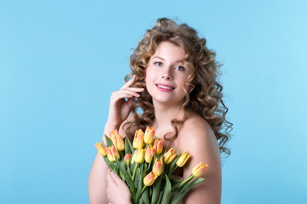 Schöne Frau mit dem lockigen Haar mit einem Blumenstrauß auf einem blauen Hintergrund.