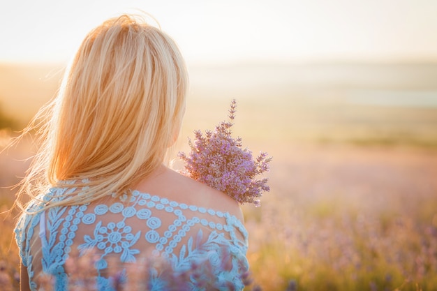 Schöne Frau mit einem Blumenstrauß des Lavendels den Sonnenuntergang genießend