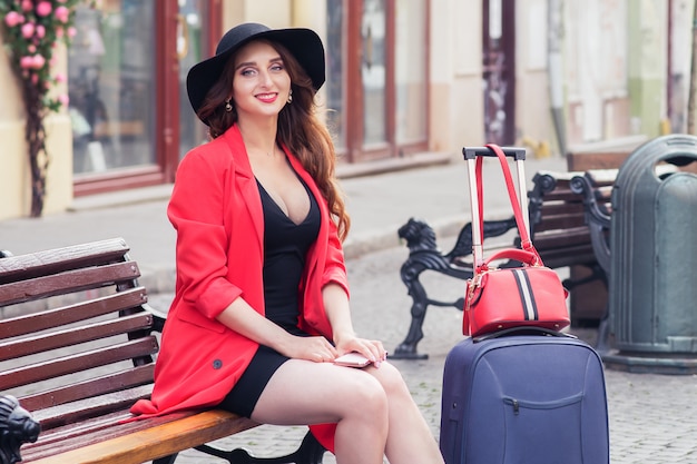 Schöne Frau mit einem Koffer, der auf einer Bank sitzt