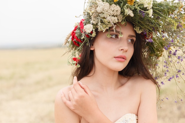 Schöne Frau mit einem Kranz auf dem Kopf, der in einem Feld in Blumen sitzt. Das Konzept von Schönheit, freiem Leben und Natürlichkeit