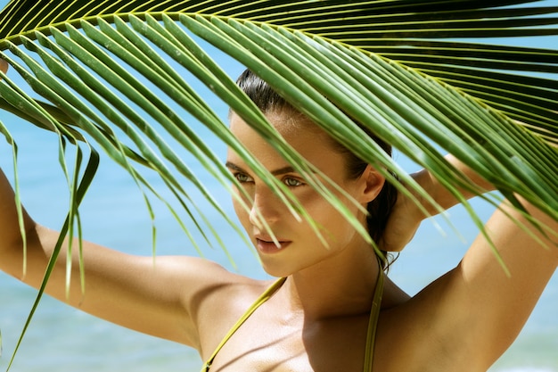 Schöne Frau mit einem Palmblatt am Strand