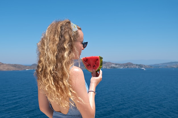 Schöne Frau mit einer Scheibe der roten Wassermelonenscheibe der Wassermelone mit Meerblick