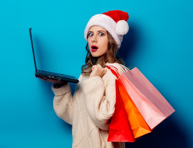 Schöne Frau mit Einkaufstaschen und Laptop-Computer auf blauer Wand