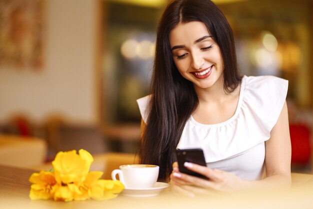 Schöne Frau mit Frühlings-Tulpenblumen im Café Frau, die Kaffee trinkt und das Telefon benutzt