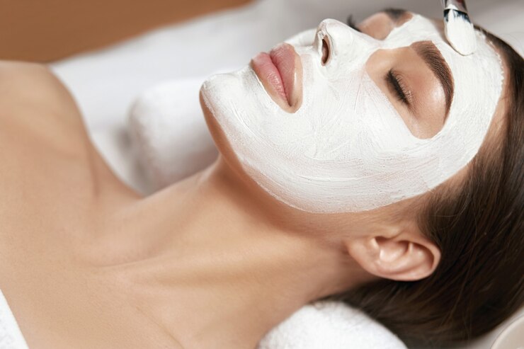 Schöne Frau mit Gesichtsmaske aus weißem Ton im Beauty Spa Salon