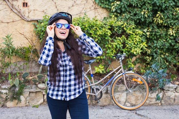 Schöne Frau mit Helm setzte Sonnenbrille mit Fahrrad auf Straße auf