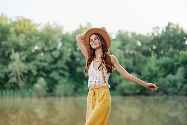 Schöne Frau mit Hut und Ökodress-Hippie-Look draußen am See beim Spazierengehen