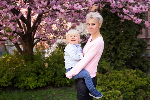 Schöne Frau mit kleinem Jungen, die Spaß in der Nähe von rosa blühendem Sakura-Baum hat Frühlingskonzept