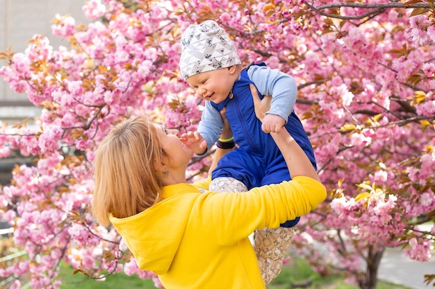 Schöne Frau mit kleinem Jungen in der Nähe von rosa blühendem Sakura-Baum Frühlingskonzept