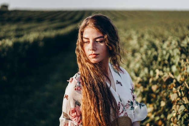 Schöne Frau mit langem lockigem Haar und Sommersprossengesicht auf Johannisbeerfeld. Mädchen in einem hellen Kleid geht im sonnigen Sommertag