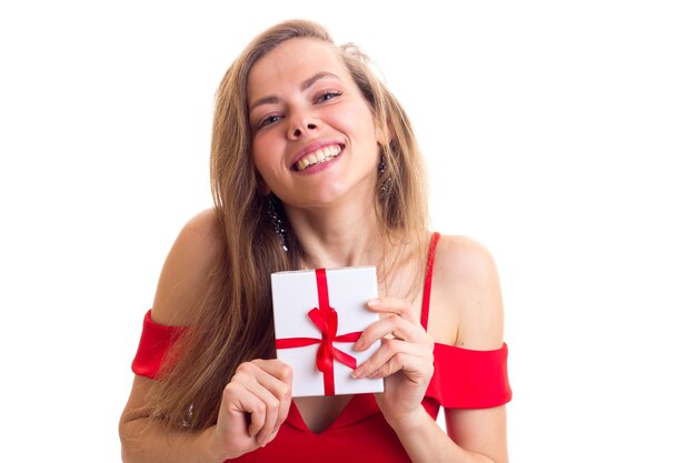 Schöne Frau mit langen braunen Haaren in einem knappen roten Kleid mit schwarzen Ohrringen, die ein kleines Geschenk halten