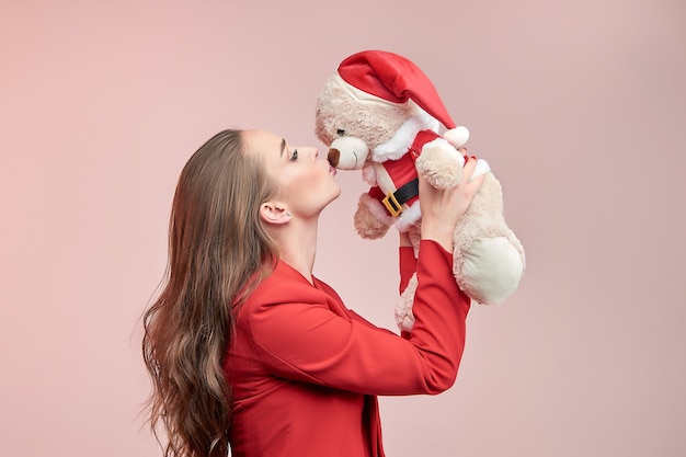 Schöne Frau mit langen gewellten Haaren küsst einen Spielzeugbären im Bild des Weihnachtsmannes.