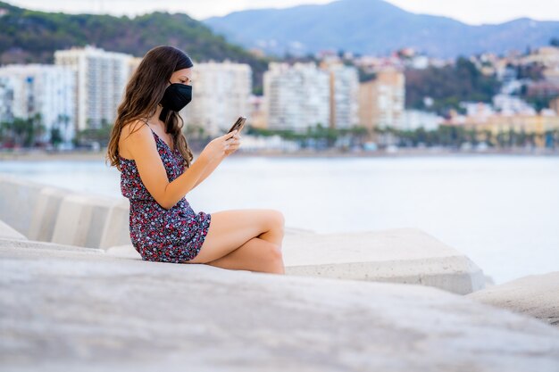 Schöne Frau mit langen Haaren benutzt das Telefon im Hafen mit Hintergrundmeer