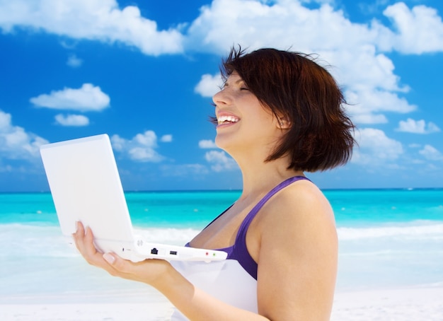 schöne Frau mit Laptop am Strand