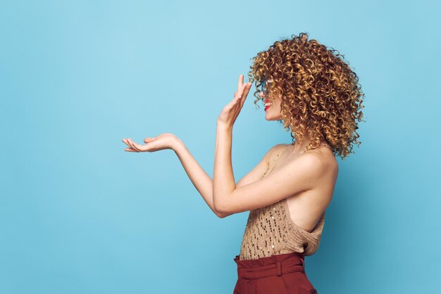 Schöne Frau mit lockigem Haar, Seitenansicht, Handbewegungen, blauer Hintergrund, Studio-Kopierraum