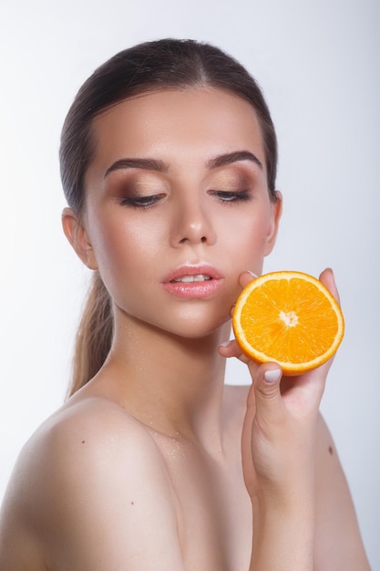 Schöne Frau mit natürlichem Make-up und Orange auf weißem Hintergrund