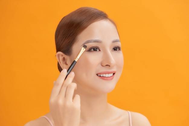 Schöne Frau mit Pinsel für Lidschatten. Foto der Frau mit perfektem Make-up auf gelber Wand. Schönheitskonzept