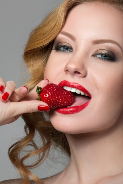 Schöne Frau mit saftigem Sommer Make-up essen rote Erdbeere