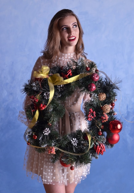 Schöne Frau mit Weihnachtskranz in den Händen auf blauem Hintergrund