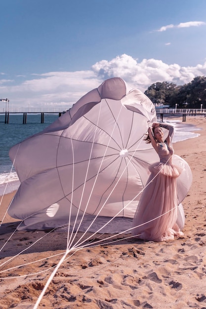 Schöne Frau mit weißem Fallschirm am Strand