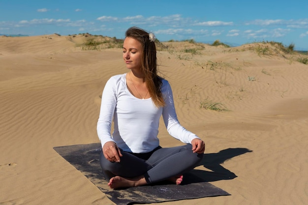 Schöne Frau mit Yogamatte, die auf Dünen sitzt