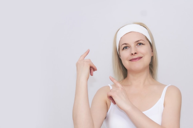 Schöne Frau mittleren Alters in einem Haarband für Schönheitsbehandlungen zeigt den Raum neben ihr