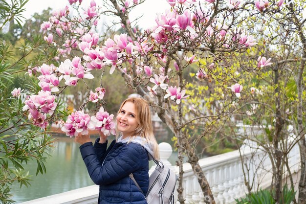 Schöne Frau nahe einem blühenden Magnolienbaum, der Kamera betrachtet lächelnd