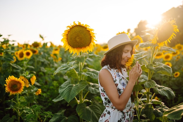 Schöne Frau posiert in einem Feld von Sonnenblumen in einem Kleid und Hut Mode-Lifestyle-Konzept