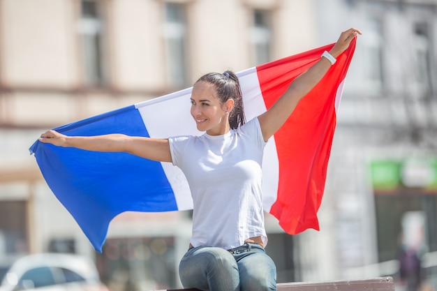 Schöne Frau schaut lächelnd zur Seite und hält eine Flagge Frankreichs hinter sich.