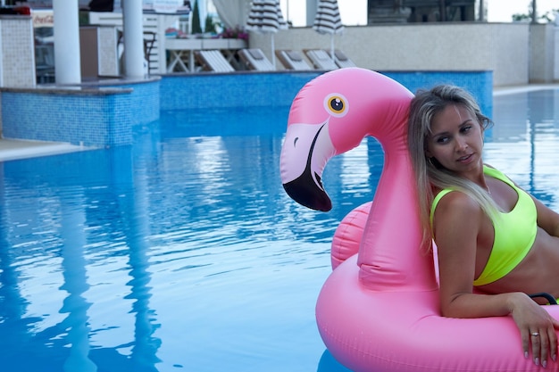 Schöne Frau schwimmt auf einem rosa aufblasbaren Flamingo im Hotelpool