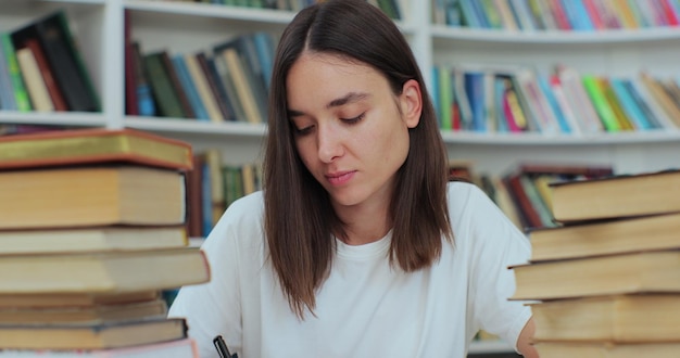 Schöne Frau sitzt am Tisch in der Universitätsbibliothek und liest ein Buch Sie ist müde und erschöpft, schüttelt den Kopf und schreibt in Copybook Selbstbildungskonzept