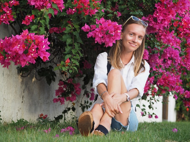 Schöne Frau sitzt auf dem Gras in der Nähe von blühenden Büschen von Blumen