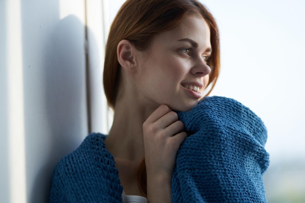 Schöne Frau sitzt auf der Fensterbank mit einem blauen Plaid