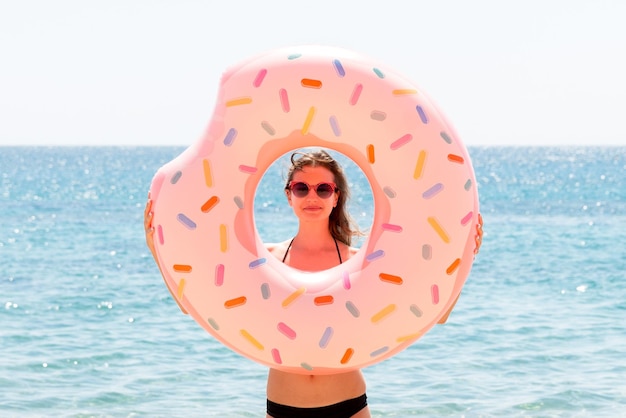 Schöne Frau spielt mit Donut-Gummiring am Strand am Meereshintergrund