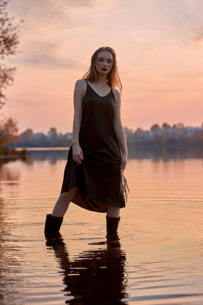 Schöne Frau steht im Wasser in einem Teich bei Sonnenuntergang