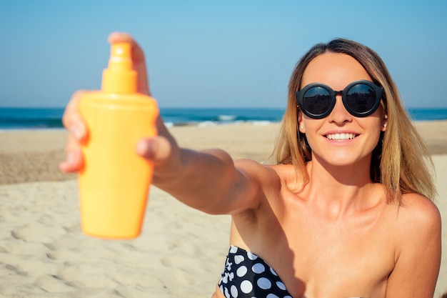 Schöne Frau streut einen Sonnenspray auf den Strand