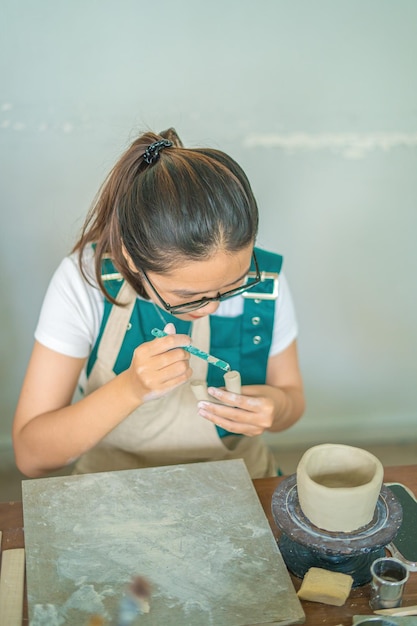 Foto schöne frau töpfer arbeiten an der töpferscheibe machen keramiktopf aus ton in töpferwerkstatt focus hand junge frau anbringen ton produktteil an zukünftigen keramikprodukt töpferwerkstatt