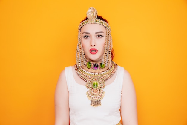 Schöne Frau wie Kleopatra im alten ägyptischen Kostüm verwirrt und überrascht auf Orange