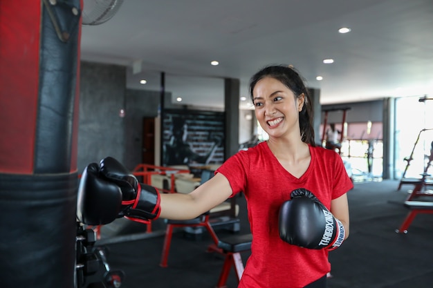 Schöne Frauen asiatischer Boxer glücklich und Spaß beim Fitnessboxen und Stanzen einer Tasche mit dem Tragen von Boxhandschuhen.