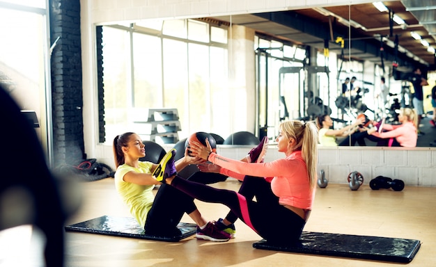 Schöne Frauen, die Dehnungsübungen mit Fitnessball im Fitnessstudio machen.