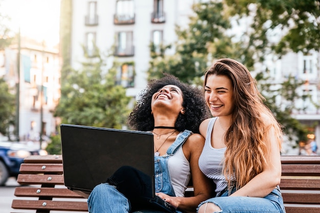 Schöne Frauen, die einen Laptop in der Straße benutzen. Jugendkonzept.