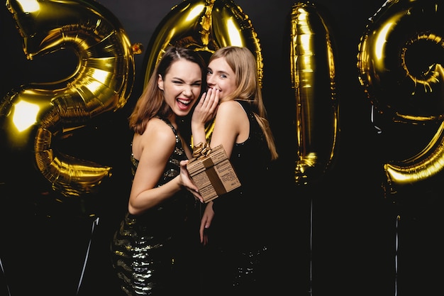 Schöne Frauen, die neues Jahr feiern. Glückliche wunderschöne Mädchen in stilvollen sexy Partykleidern, die Goldballons 2019 halten und Spaß auf der Silvesterparty haben. Feiertagsfeier. Hochwertiges Bild