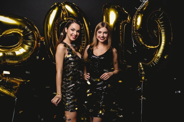 Schöne Frauen, die neues Jahr feiern. Glückliche wunderschöne Mädchen in stilvollen sexy Partykleidern, die Goldballons 2019 halten und Spaß auf der Silvesterparty haben. Feiertagsfeier. Hochwertiges Bild