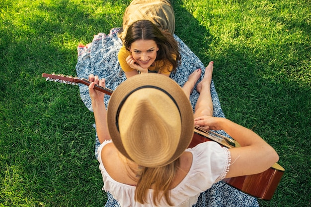 Schöne Frauen, die Spaß haben, Gitarre im Park zu spielen. Freunde und Sommerkonzept.