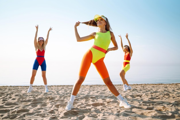 Schöne Frauen in Badeanzügen tanzen am Strand. Fitnesstraining, Aerobic und People-Konzept
