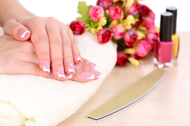Schöne Frauenhände mit französischer Maniküre und Blumen auf dem Tisch in der Nähe